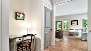 Un couloir avec un bureau, une chaise et une porte donnant sur une pièce où se trouvent un canapé et une fenêtre.