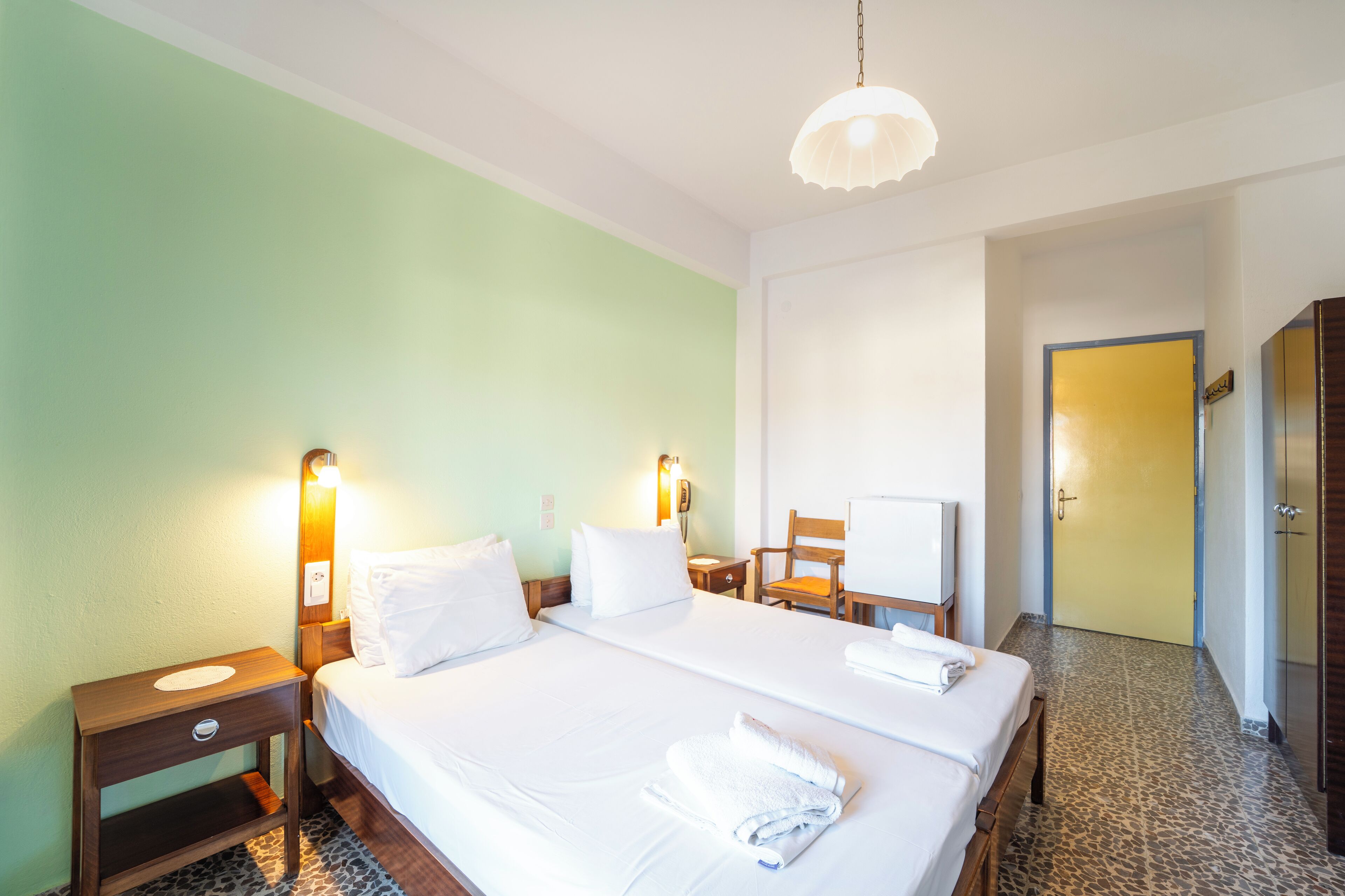 A hotel room with two beds, a desk, a chair, a TV, and a wardrobe.