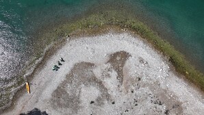 Luchtbeeld van een strand met helder turquoise water, een zandgebied met een kano en een klein bootje.