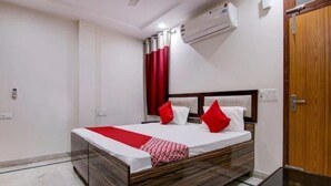 A hotel room with a bed, a wooden headboard, a red and white bedspread, and an air conditioning unit on the wall. - Roomshala 095 Shyam Villa (New Delhi)