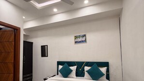 A modern bedroom with a bed, a ceiling fan, recessed lighting, a wardrobe, and a painting on the wall. - Roomshala 095 Shyam Villa (New Delhi)