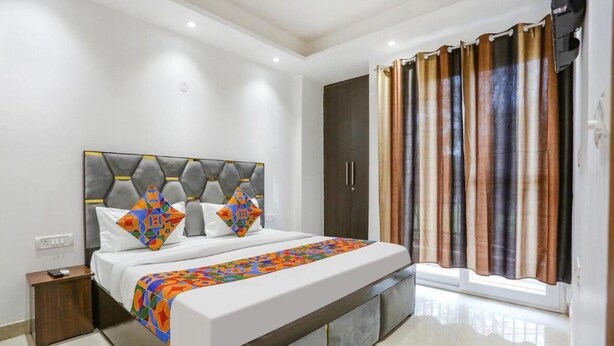 A modern bedroom with a large bed, a headboard with geometric patterns, a wardrobe, and a window with curtains. - Roomshala 095 Shyam Villa (New Delhi)