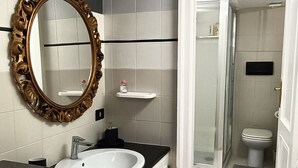 A bathroom with a white sink, a large ornate mirror, and a shower area visible through an open door. - Contemporary Art apartments by Spanish steps, Cozy space in the center of Rome. (Roma)