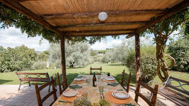 An outdoor dining area with a table set for six, surrounded by wooden chairs, under a bamboo roof. - Big Family Villa in Rome Countryside (Rocca di Papa)