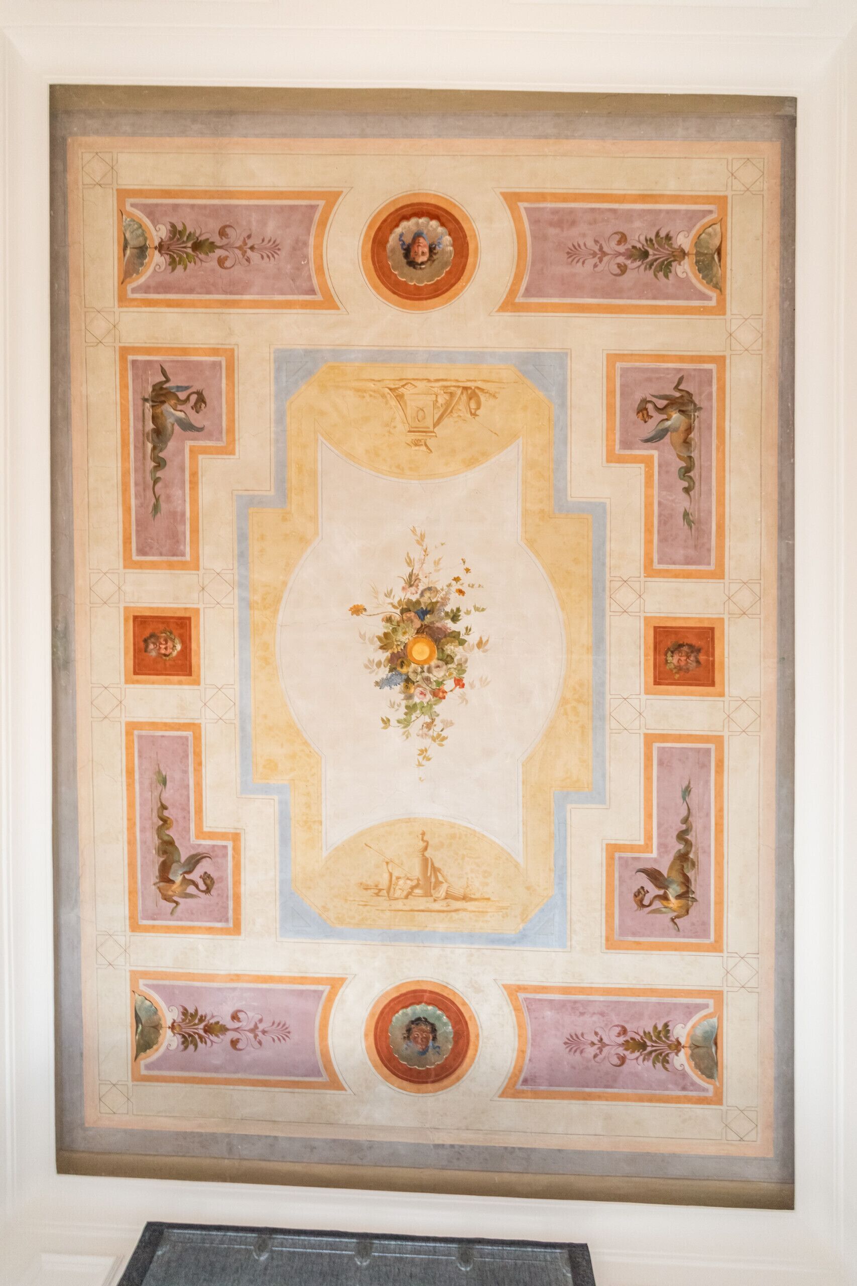 A ceiling with a central floral motif surrounded by geometric patterns and decorative elements.