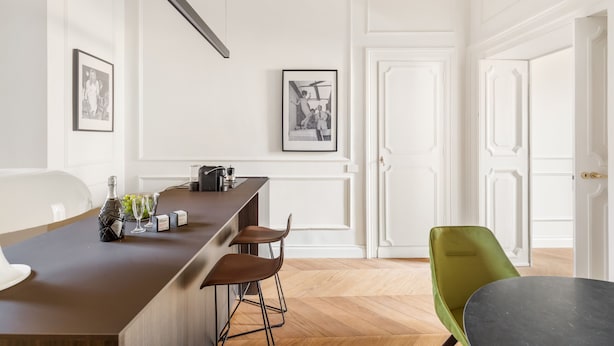 A modern kitchen with a bar area, white cabinetry, and a dining area with a green chair. - Charm and Style by The Spanish Steps (Roma)