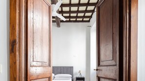 A wooden door opening to a bedroom with a bed, a nightstand, and a ceiling fan.