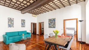 A spacious living area with a wooden dining table, a teal sofa, and a grey armchair.