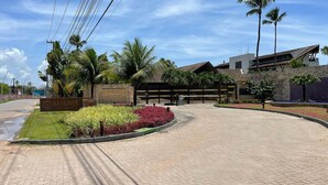 Une allée d’accès pavée, agrémentée d’un panneau indiquant « Malawi », entourée de palmiers et de parterres de fleurs aménagés.