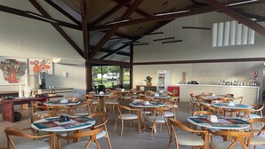 Un café spacieux avec des tables et des chaises en bois, un coin bar et des œuvres d’art accrochées aux murs.
