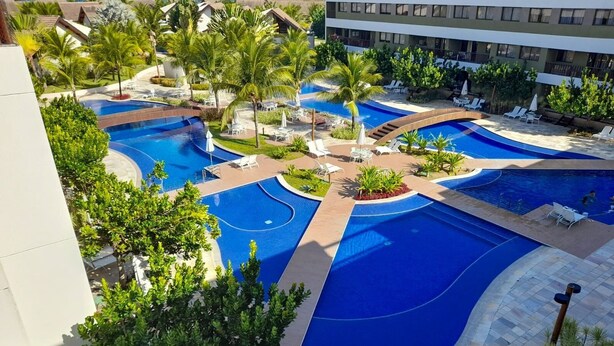 Un complexe hôtelier doté de plusieurs piscines, de palmiers et d’espaces de détente.