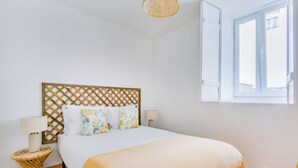 A bedroom with a bed, a wooden headboard, a bedside table, a lamp, and a window with blinds. - Casa de Santana (Lisbon)
