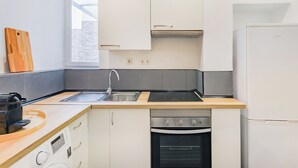 A compact kitchen with white cabinets, a stainless steel sink, a built-in oven, and a white refrigerator. - Casa de Santana (Lisbon)