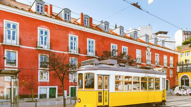 A yellow tram on tracks with a red building in the background. - Casa de Santana (Lisbon)