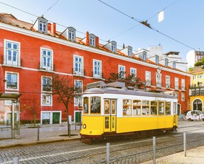 Um elétrico amarelo sobre trilhos, com um edifício vermelho ao fundo.