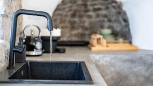 Un évier de cuisine avec un robinet moderne, une bouilloire et un mur en pierre en arrière-plan.
