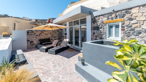 Une terrasse extérieure moderne, dotée d’un sol en pierre, d’un espace salon avec des coussins et d’un grand parasol.