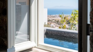 Une vue depuis une fenêtre donnant sur une piscine, avec un paysage lointain et des montagnes en arrière-plan.