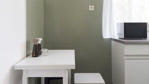 Ett litet pentry med en vit bänkskiva, en mikrovågsugn och ett grönt kakel på väggen bakom. Där finns två barstolar och ett litet bord.