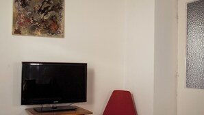 Ett rum med en tv på ett träställ, en röd stol, en vit taklampa och en väggpanel med en tydlig struktur.