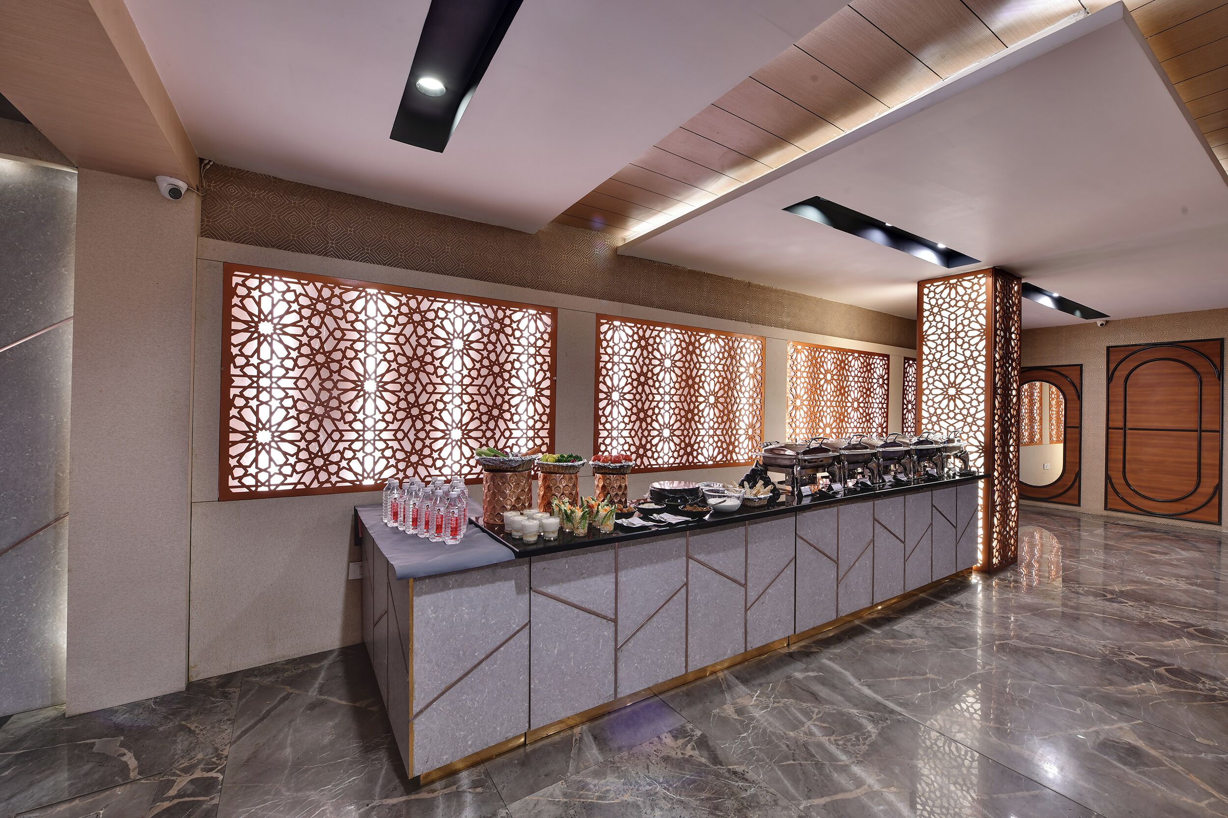 Un moderno vestíbulo de hotel con piso de mármol, un mostrador de recepción con un panel decorativo y una pared divisoria de madera.