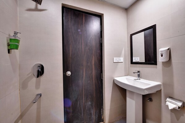 A bathroom with a dark wooden door, a white sink, a mirror, a soap dispenser, and a toilet paper holder.