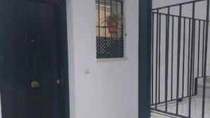 A hallway with a dark wooden door, a small window with a potted plant, and a metal railing. - Apartamento Barrio Santa Cruz, Centro Sevilla (Sevilla)