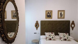 A bedroom with a large ornate mirror, a tufted headboard, two framed pictures, and a small round table. - Apartamento Barrio Santa Cruz, Centro Sevilla (Sevilla)