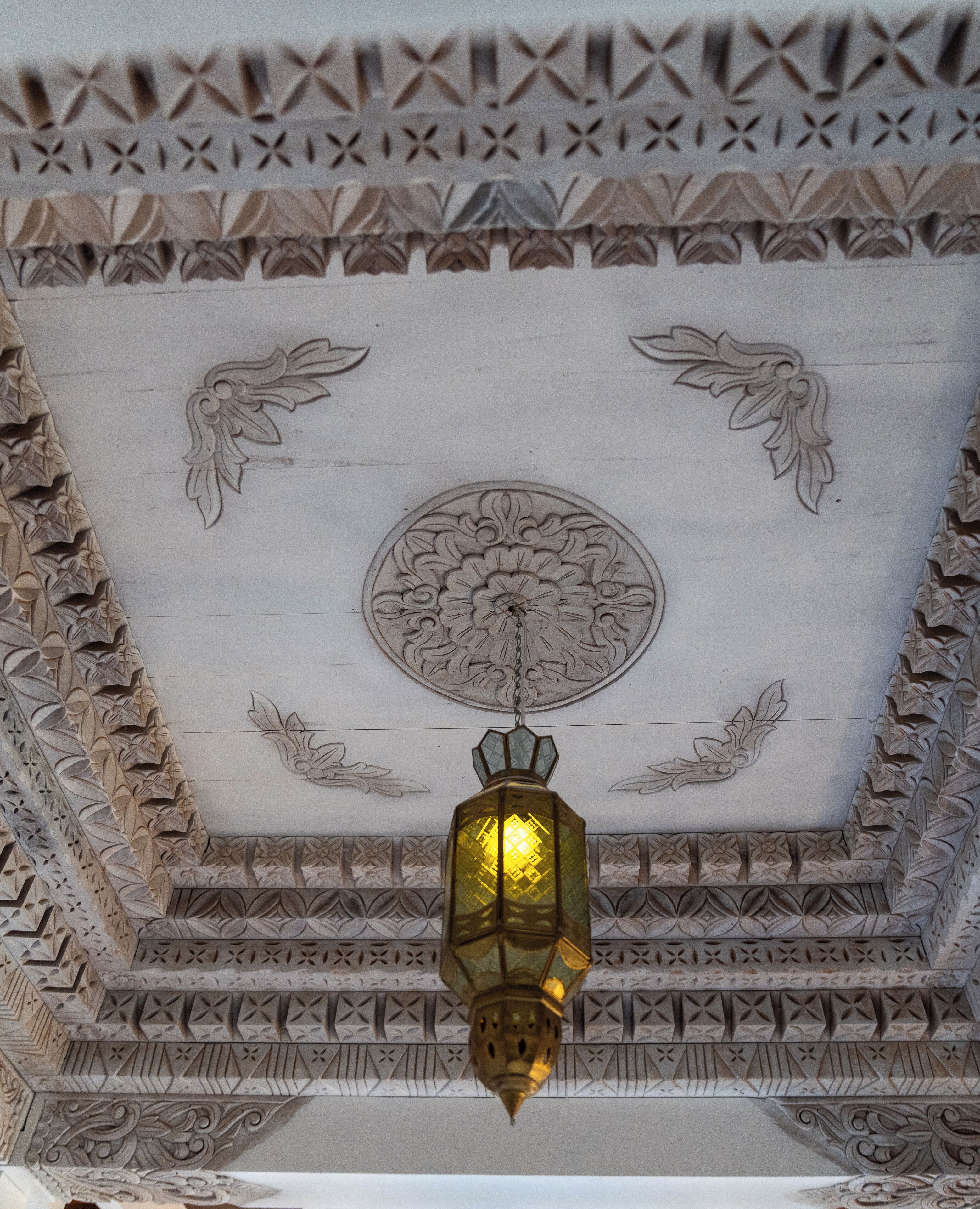 A detailed ceiling with intricate floral and geometric patterns, a central circular medallion, and a hanging lantern.