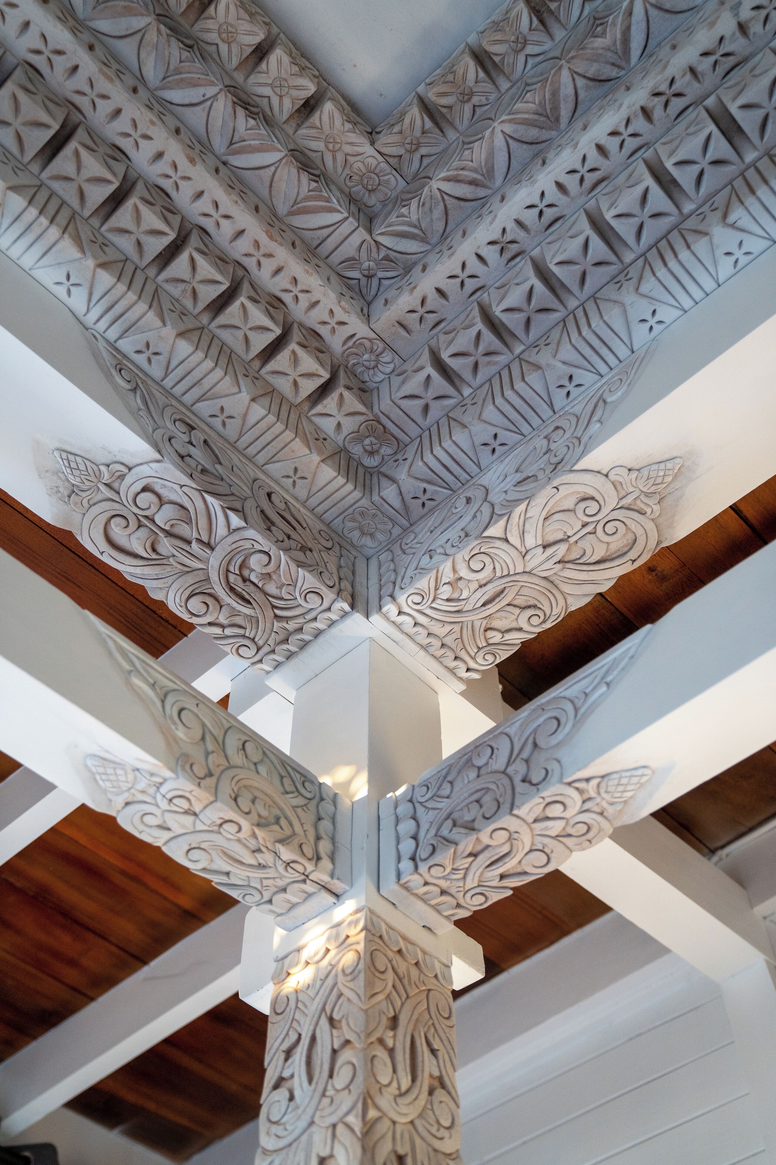 A ceiling with intricate geometric and floral carvings, wooden beams, and a white column with a detailed base.