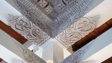 Techo con elaboradas esculturas geométricas y florales, vigas de madera y una columna blanca con una base detallada.
