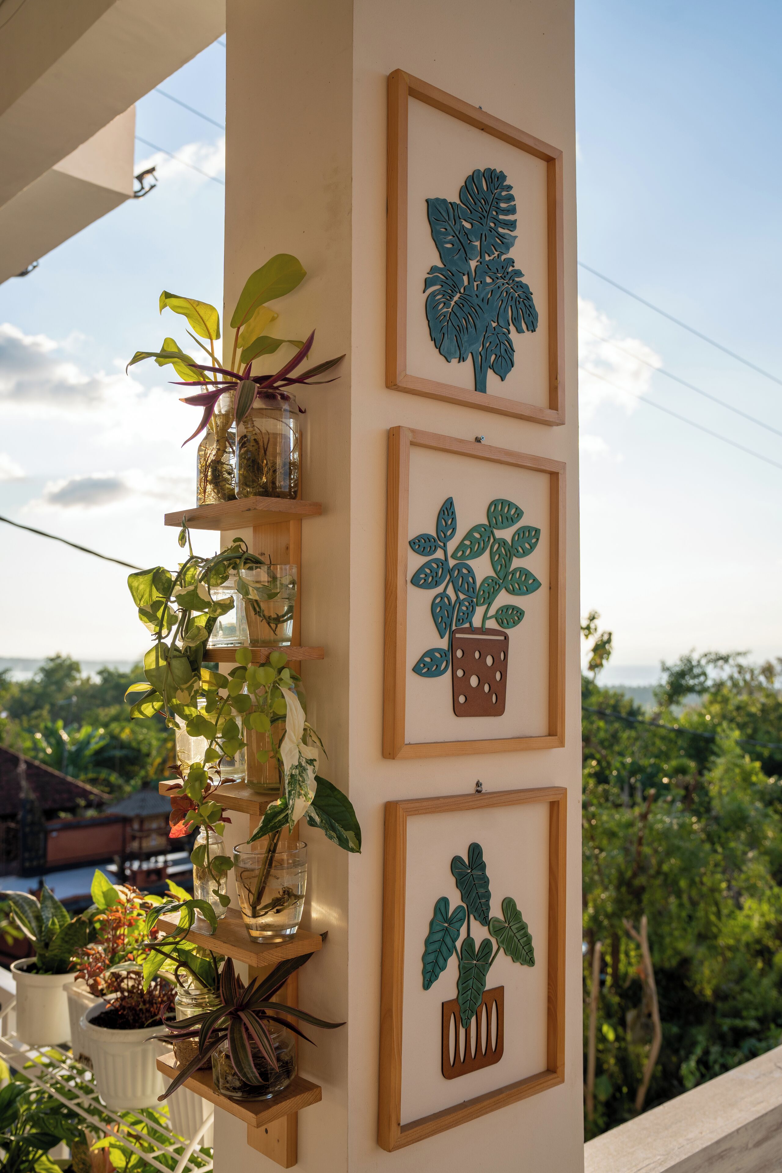 A vertical arrangement of potted plants and framed artwork on a balcony railing.