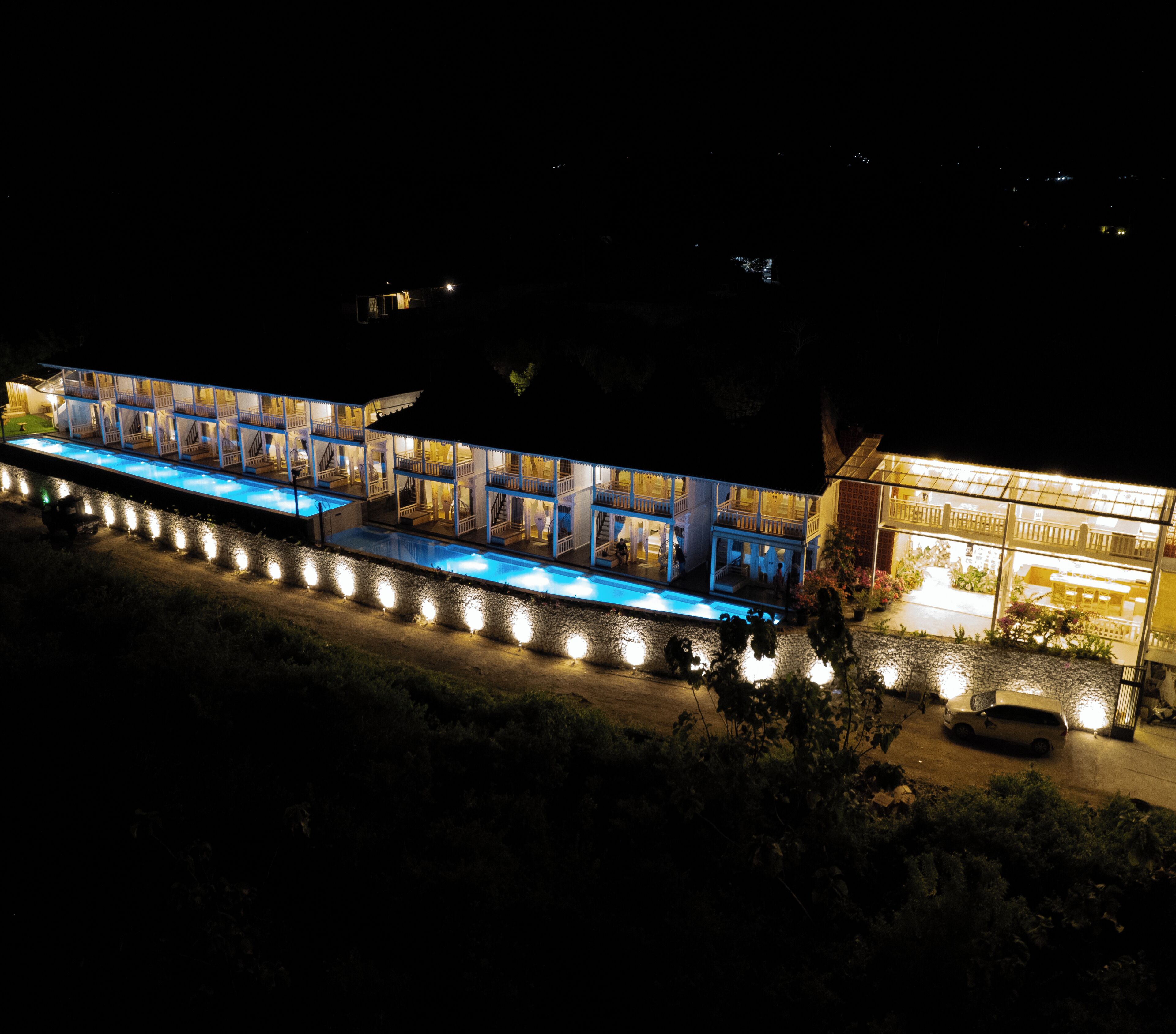 A multi-story hotel with a pool area, outdoor seating, and a well-lit entrance.