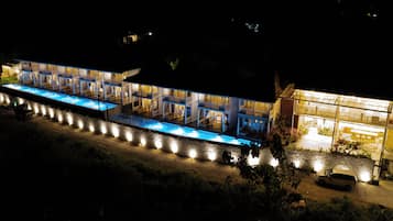 A multi-story hotel with a pool area, outdoor seating, and a well-lit entrance.