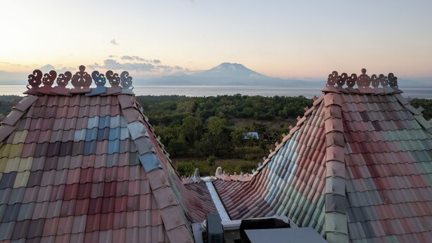 A traditional roof with decorative elements and a view of a mountain and water body. - Mambo Hill Resort (Penida Island)