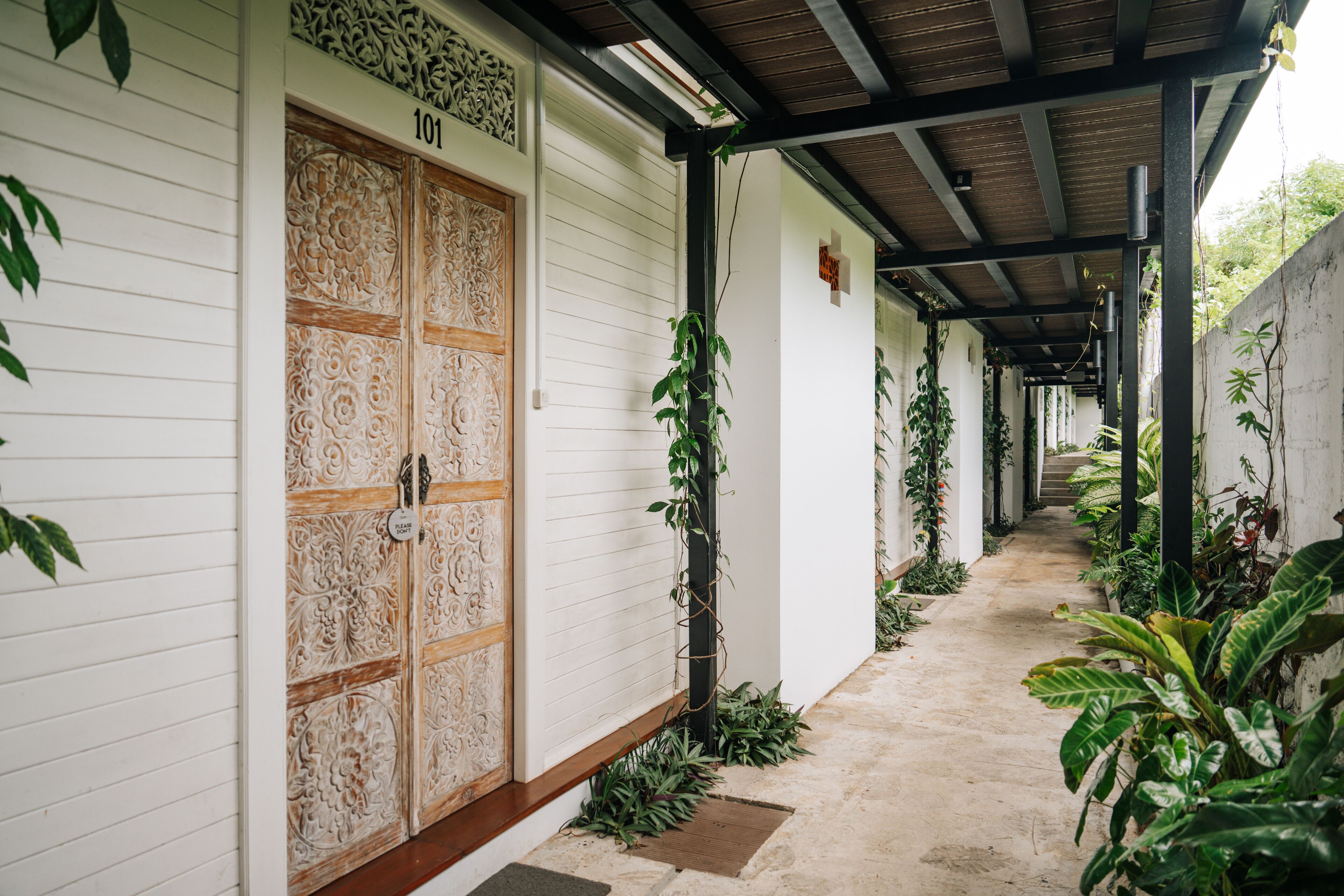 A corridor with a wooden door marked "101" and a covered walkway with plants.