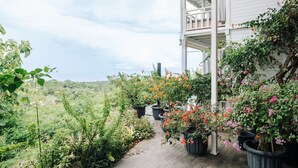 A covered porch with potted plants and flowers, leading to a white house with a balcony. - Mambo Hill Resort (Penida Island)