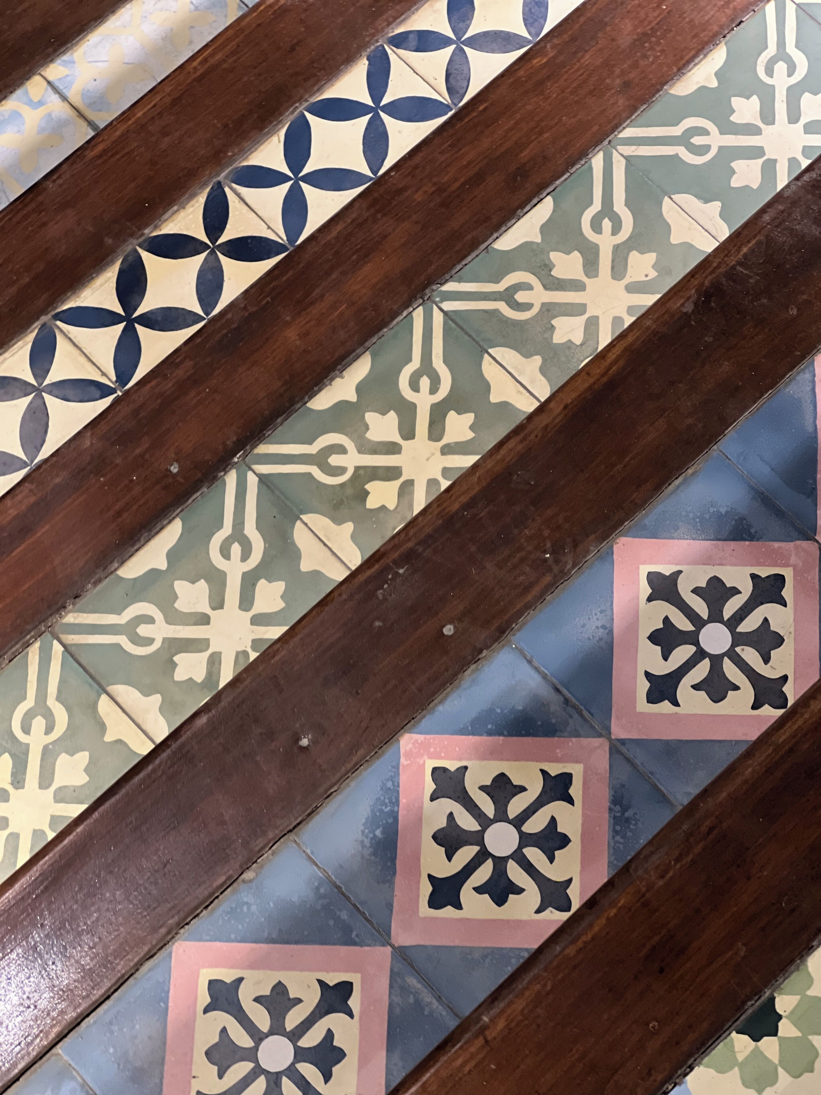 A close-up of a tiled floor with geometric patterns and a wooden floorboard.