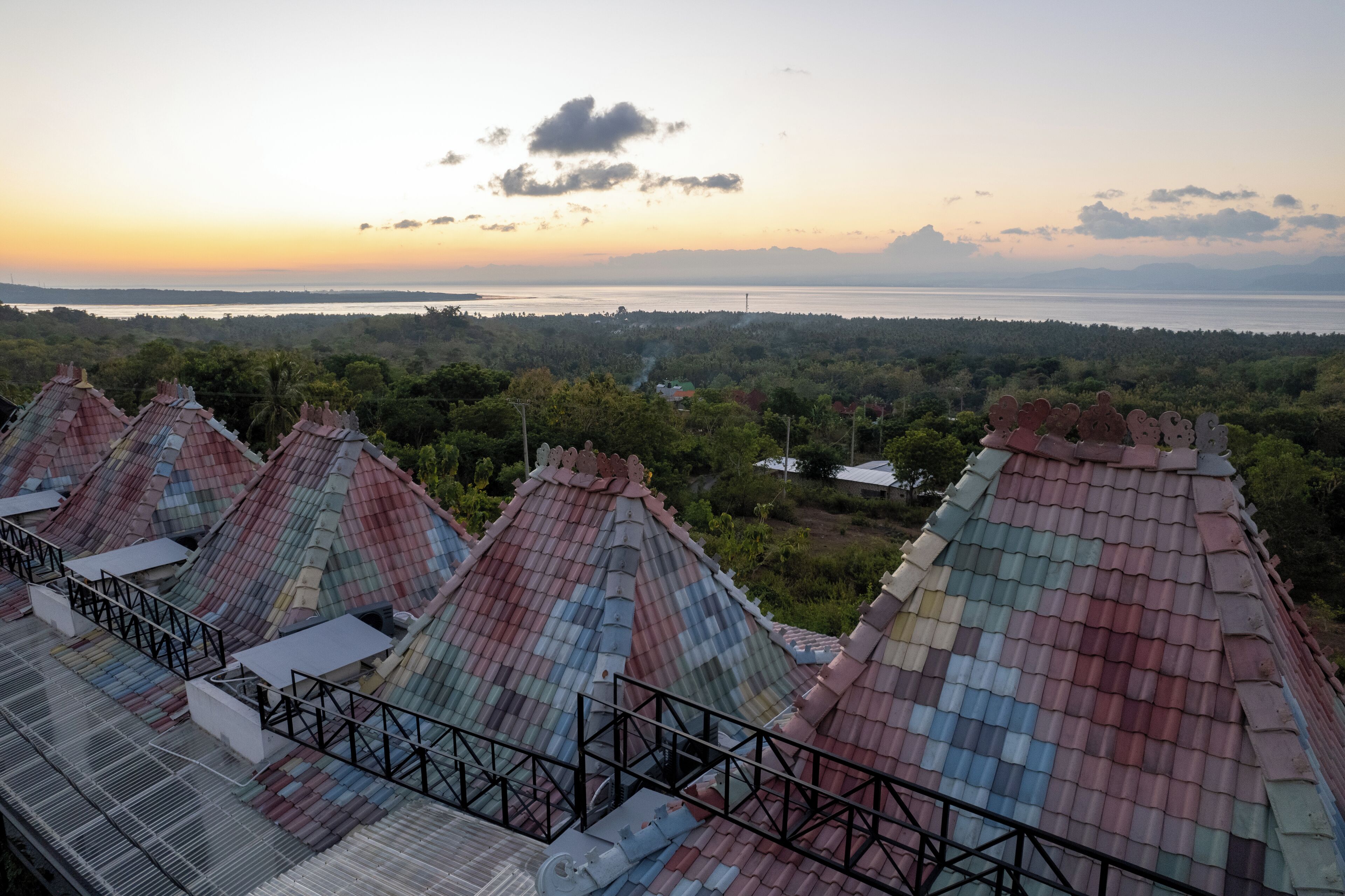 A row of colorful, traditional-style buildings with a view of a forested area and a body of water in the distance.