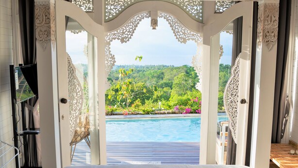 A bedroom with a large bed, a view of a swimming pool, and intricate ceiling designs. - Mambo Hill Resort (Penida Island)