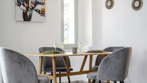A dining area with a wooden table, four grey chairs, and a vase with a bowl and wine glasses. - Geminos Complex Villas - Standard Villa (Santorini)