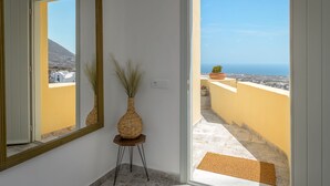A room with a large mirror, a vase with dried plants, and a view of the sea through an open door. - Geminos Complex Villas - Standard Villa (Santorini)