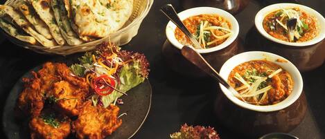 Une table garnie de différents plats, notamment du pain naan, une salade et plusieurs bols de curry.