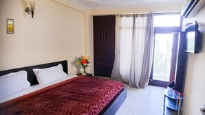 Quarto com cama, mesa de cabeceira, televisão, guarda-roupa e janela com cortinas.