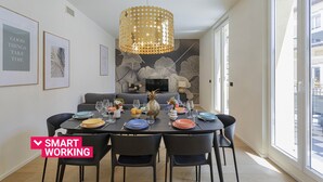 Un coin repas avec une table dressée pour six personnes, un lustre moderne et un canapé en arrière-plan.