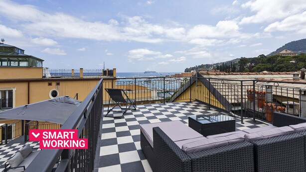 Une terrasse sur le toit, dotée d’un sol à carreaux, de mobilier d’extérieur et offrant une vue sur la mer et les bâtiments éloignés.