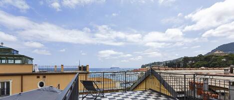 Una terraza en la azotea con piso a cuadros, mobiliario exterior y vistas al mar y edificios al fondo.