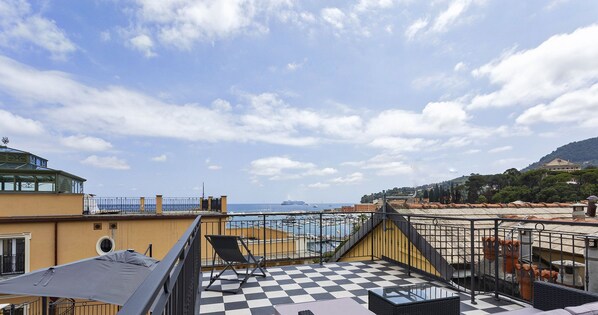 Une terrasse sur le toit, dotée d’un sol à carreaux, de mobilier d’extérieur et offrant une vue sur la mer et les bâtiments éloignés.