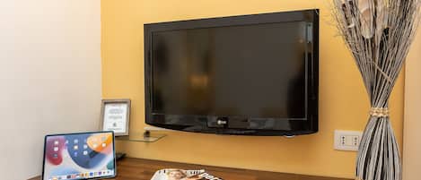 A flat-screen TV mounted on a yellow wall, a tablet on a wooden table, and a magazine on the table.