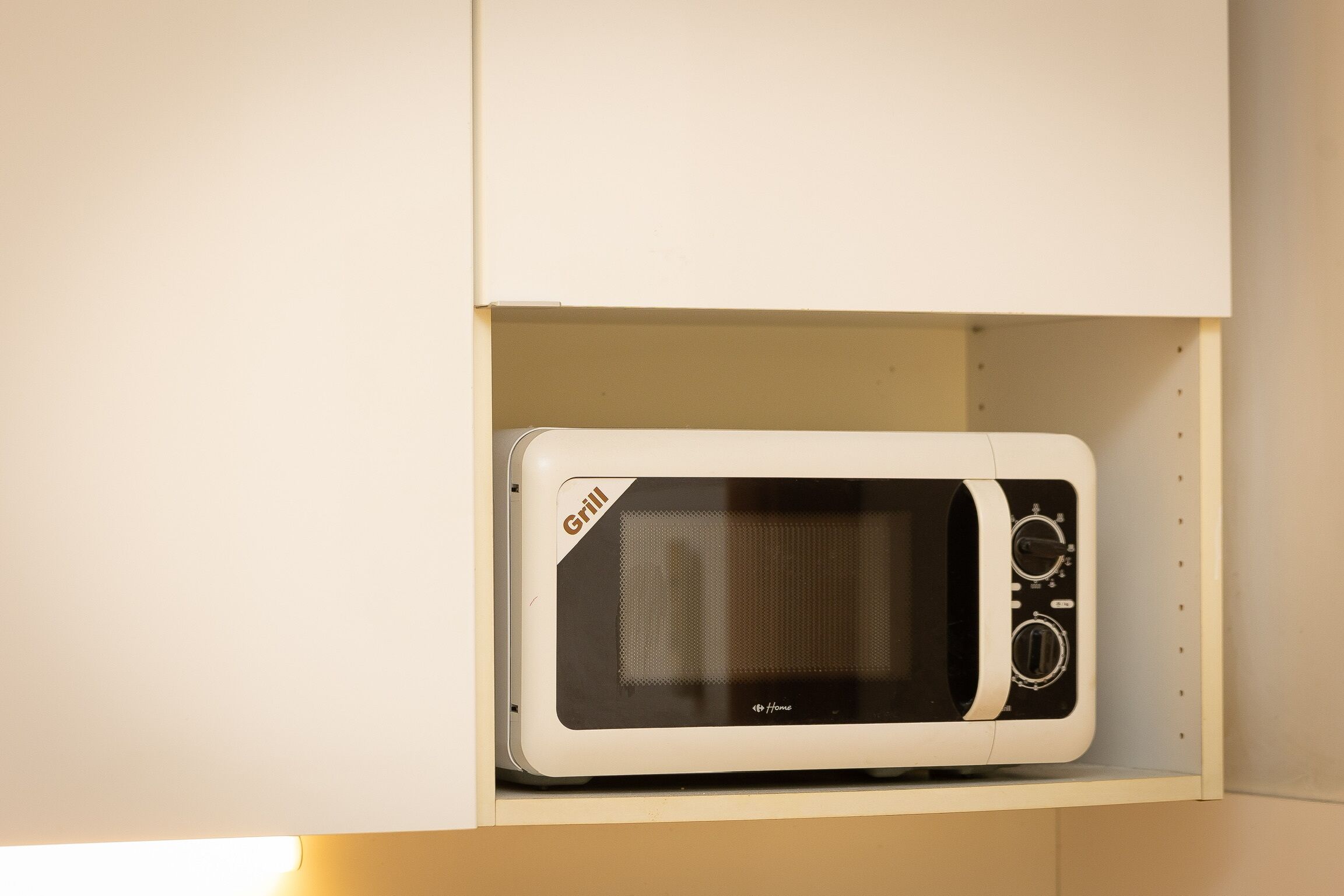 A microwave in a white cabinet with a grill label.